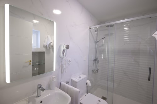 Baño moderno del Hotel Boutique Alcazaba Salobreña con espejo iluminado, accesorios blancos y cabina de ducha de vidrio