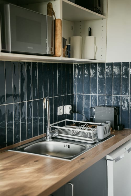 Kitchenette studio avec crédence carrelée foncée, comptoir bois, évier, égouttoir et appareils modernes à Ô Coeur de