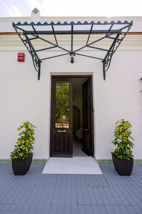 Elegante entrada del Hotel Alcazaba Salobreña con toldo azul ornamentado, puerta de madera oscura y macetas en piso blanco