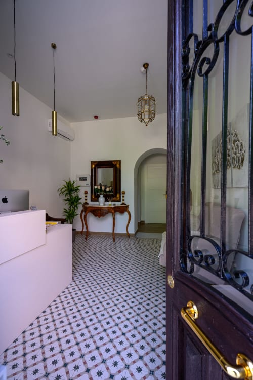 Elegante vestíbulo de hotel con suelo de azulejos geométricos, lámparas colgantes de latón, espejo ornamentado y puerta de arco en Alcazaba Salobreña