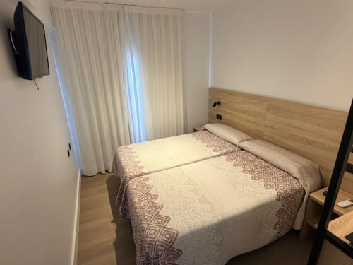 Habitación moderna en Hostal Juan Carlos de Carboneras con cama doble, cabecero de madera, TV y cortinas blancas