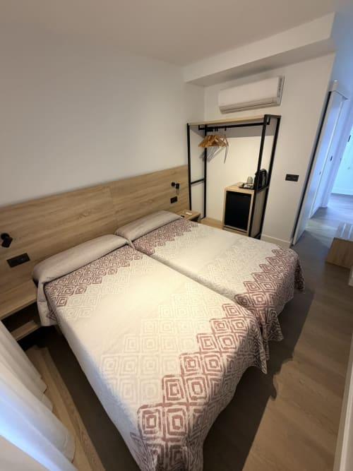 Habitación moderna en Hostal Juan Carlos de Carboneras con dos camas individuales, cabecero de madera, perchero negro y aire acondicionado