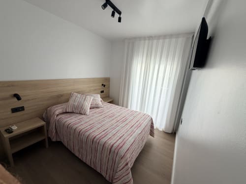 Dormitorio moderno en Hostal Juan Carlos, Carboneras, con cama de rayas, cabecera de madera, TV y acceso a terraza