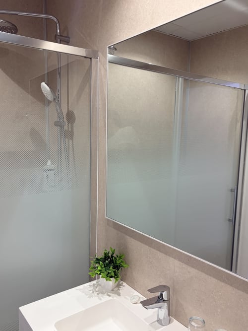 Baño moderno del Hostal Juan Carlos en Carboneras con ducha de cristal, lavabo blanco y paredes con azulejos beige