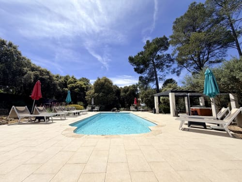 Sunny swimming pool at CARPE DIEM hotel in Lorgues surrounded by loungers, umbrellas, and lush gardens
