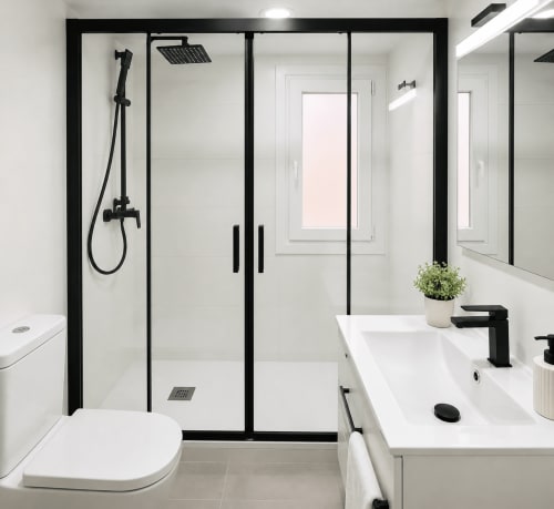 Baño moderno en apartamento de Baiona con ducha de cristal con marco negro, lavabo blanco, inodoro y espejo con vistas a la ciudad