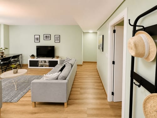 Sala de estar moderna en Baiona con sofá gris, televisor, pisos de madera y sombreros de paja en perchero