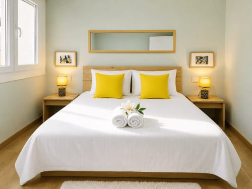 Habitación moderna y luminosa en Holibai, Baiona, con cojines amarillos, ropa de cama blanca, muebles de madera e iluminación cálida