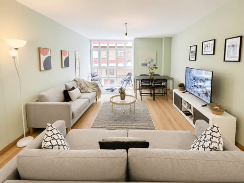 Moderno salón en apartamento de Baiona con sofás crema, televisor, comedor y vistas a la ciudad por amplios ventanales