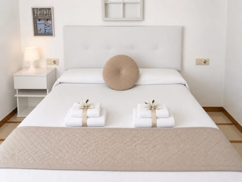 Elegante dormitorio de apartamento en Baiona con ropa de cama blanca, almohada circular beige y toallas dobladas en la cama