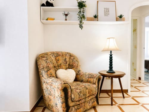 Acogedor salón del apartamento Mencer en Baiona con sillón floral, cojín blanco con corazón, mesa de madera y lámpara