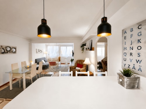 Moderna zona de cocina-comedor en el apartamento Holibai, Baiona, con lámparas colgantes negras y salón abierto