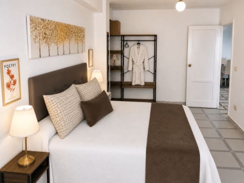 Dormitorio moderno en apartamento Holibai, Baiona con cama blanca, cabecero oscuro, obra de arte dorada y armario abierto