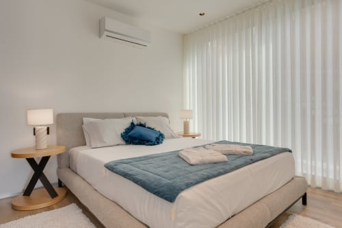 Modern bedroom at BHF Residences in Arco da Calheta with gray upholstered bed, white linens, and floor-to-ceiling curtains