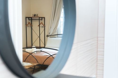 Camera da letto presso Elite Apartment SPA Catania con attaccapanni in metallo, grucce in legno e finestra con tende color crema