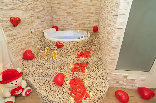 Bagno romantico con petali di rosa rossa, decorazioni a cuore e vasca idromassaggio illuminata all'Elite Apartment SPA di Catania