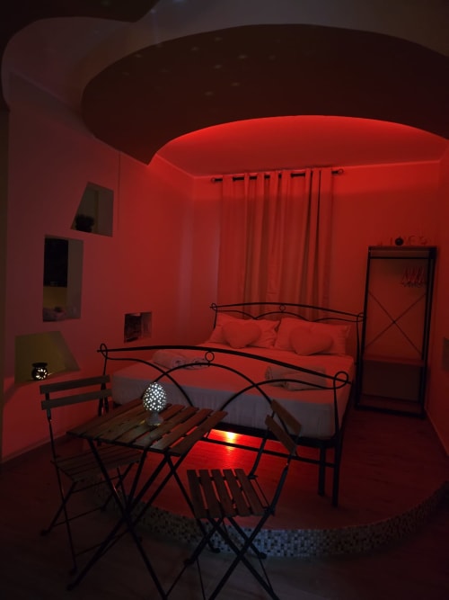 Elegante camera da letto in appartamento SPA a Catania con illuminazione rossa ambient, letto queen, struttura in metallo, area pranzo e design moderno