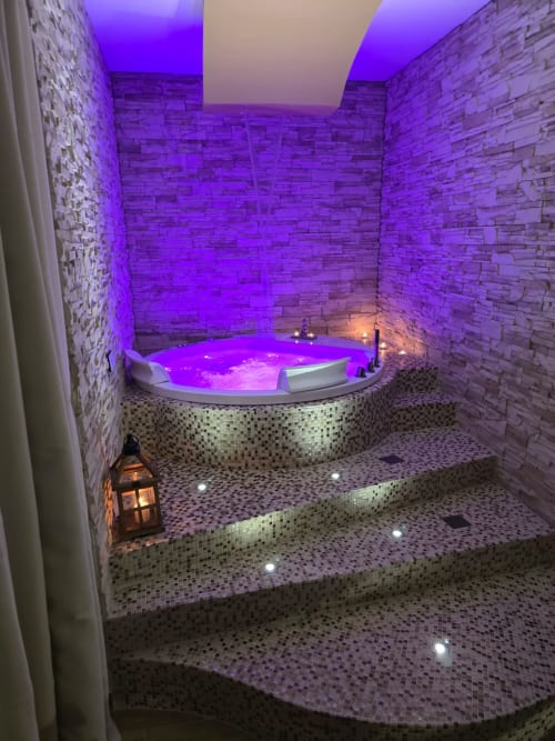 Lussuosa vasca idromassaggio con illuminazione viola presso Elite Apartment SPA, Catania. Pareti in pietra, pavimento riscaldato e illuminazione d'atmosfera.