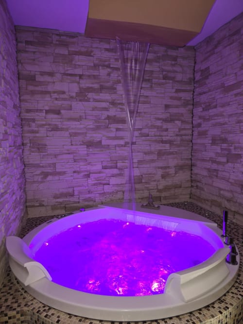 Vasca circolare lussuosa con illuminazione viola e cascata d'acqua presso l'Elite Apartment SPA di Catania