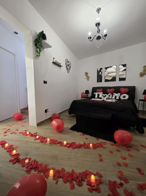 Camera romantica all'Elite Apartment SPA di Catania con petali di rosa rossa, palloncini, candele e letto king size nero