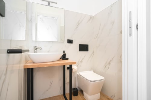 Bagno moderno dell'Elite Apartment SPA a Catania con pareti in marmo, lavabo vessel, vanità in legno e wc contemporaneo
