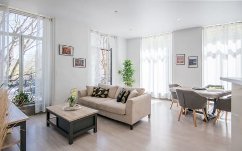 Salon moderne à Millau avec canapé beige, coin repas, grandes fenêtres et vue sur la ville