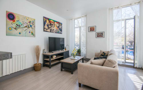 Modern living room in Le Central apartment in Millau with beige sofa, black TV stand, and large balcony overlooking city