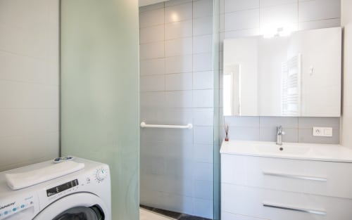 Modern bathroom with washing machine, glass shower enclosure, white vanity and mirror in Millau apartment