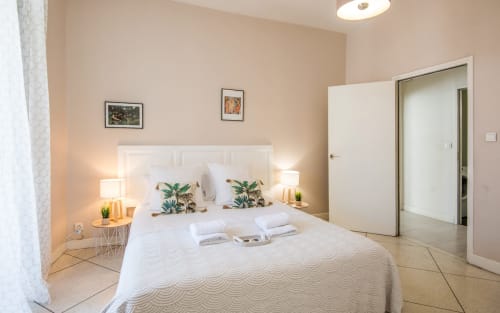 Modern bedroom in Millau city center apartment with white bed, botanical pillows, bedside lamps, and ensuite bathroom access