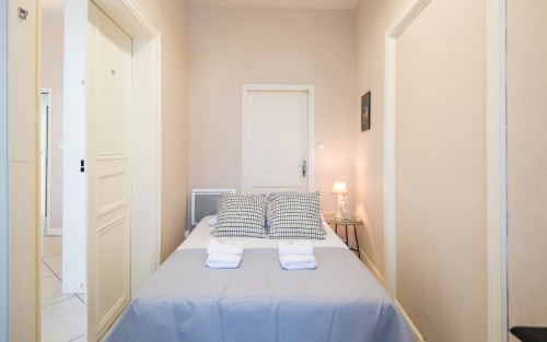 Cozy bedroom at Le Central apartment in Millau with double bed, checkered pillows, bedside lamp, and white doors leading to