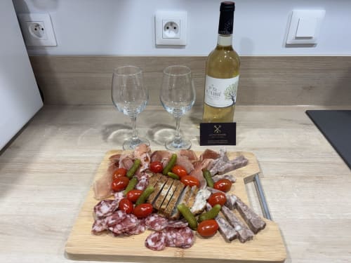 Charcuterie board with cured meats, pickles, tomatoes, wine glasses and bottle at Le Central apartment, Millau