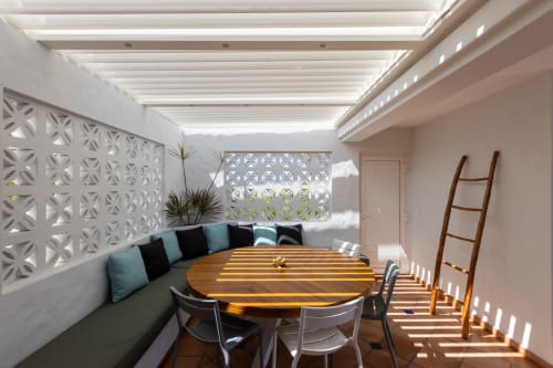 Espace de repas extérieur moderne à la Villa Agama avec table en bois, sièges aux coussins bleus et écrans blancs géométriques