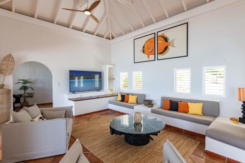 Salon moderne de la Villa Agama, Saint-Martin avec sièges gris, table ronde, œuvre orange et décoration tropicale