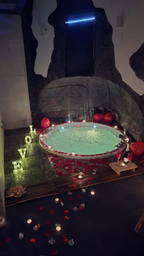 Suite spa romantica di Elite Apartment SPA Catania con vasca idromassaggio illuminata, petali di rosa rossa, candele e neon blu