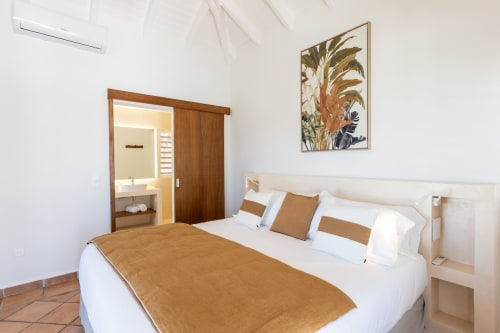 Chambre moderne à la Villa Agama à Saint-Martin avec lit queen, parure caramel, salle de bain attenante et décor tropical