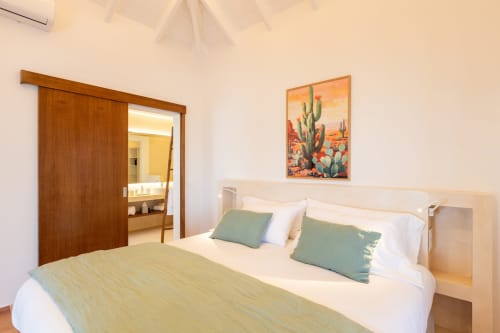 Chambre lumineuse à la Villa Agama à Saint-Martin avec lit queen-size, oreillers verts, porte coulissante en bois et décoration cactus désertique.