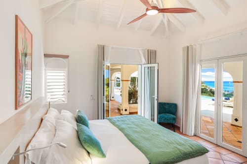 Chambre lumineuse à la Villa Agama à Saint-Martin avec vue sur l'océan, literie verte, ventilateur de plafond et accès à la terrasse