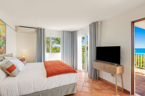 Chambre lumineuse à la Villa Agama à Saint-Martin avec vue sur l'océan, literie blanche, coussin orange et mobilier moderne