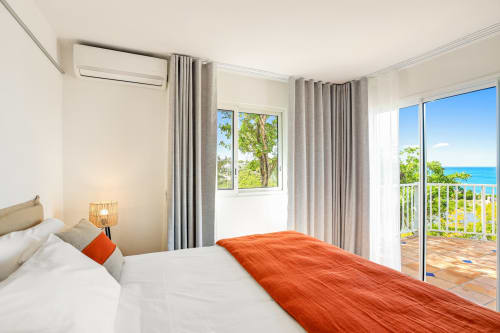 Chambre lumineuse à la Villa Agama avec vue sur l'océan, literie blanche, touches orangées et terrasse dominant Saint-Martin