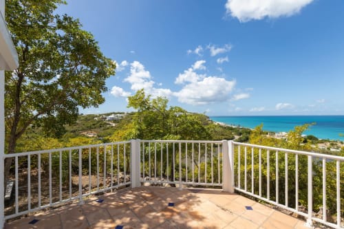 Terrasse de la Villa Agama avec vue sur la mer des Caraïbes turquoise, balustrades blanches et arbres tropicaux à Saint-Martin