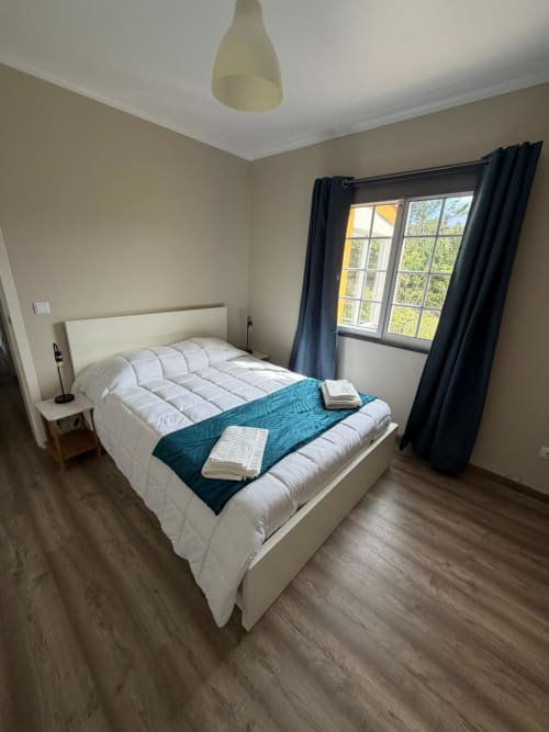 Modern bedroom at Casa da Avó Alice villa in São Roque do Pico with white bed, teal runner, windows, and black curtains