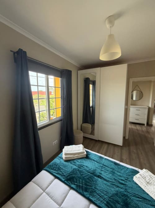 Modern bedroom at Casa da Avó Alice villa in São Roque do Pico with teal bedding, wardrobe, and city view window