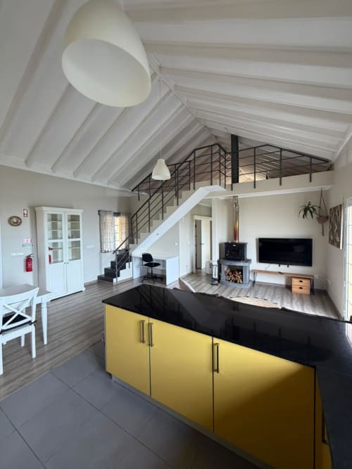 Modern villa living area at Inn Nature with yellow kitchen island, fireplace, TV, and mezzanine loft in São Roque do Pico