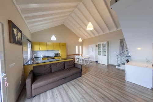 Bright open-plan villa interior with yellow kitchen, brown sofa, and vaulted ceiling at Casa da Avó Alice, São Roque do Pico