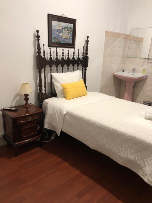 Quarto de solteiro com cama preta ornamentada, almofada amarela, criado-mudo em madeira e casa de banho partilhada na Guest House Infante Dom