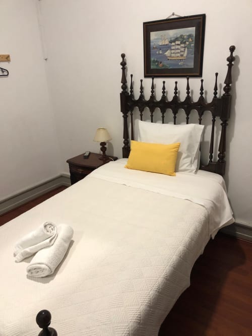 Cama individual com roupa de cama branca e almofada amarela na Pensão Infante Dom Henrique, Coimbra, com cabeceira em madeira escura