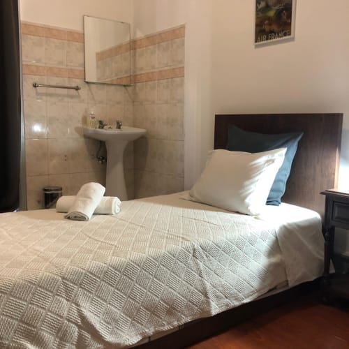 Quarto individual com casa de banho partilhada na Pensão Infante Dom Henrique, Coimbra. Cama com almofadas brancas, lavatório no quarto e