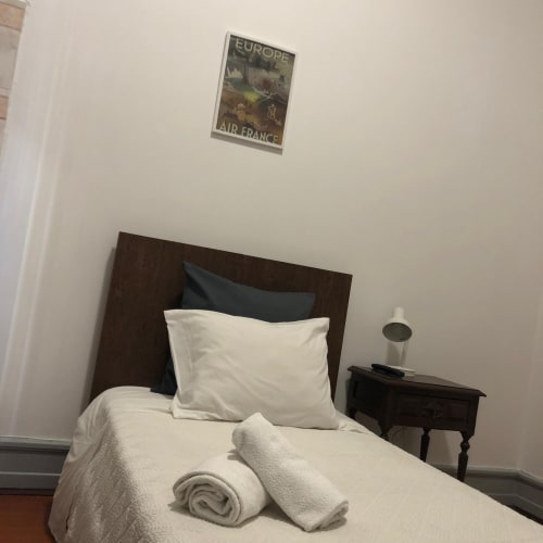 Quarto individual com roupa de cama branca, cabeceira de madeira escura e cartaz de viagem Air France na Guest House Infante Dom Henrique