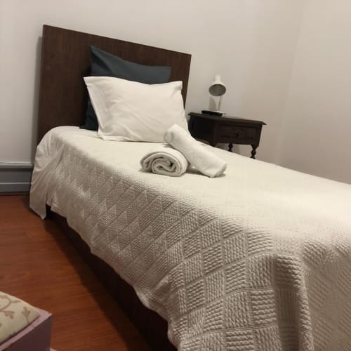 Quarto individual na Guest House Infante Dom Henrique em Coimbra com roupa de cama creme, cabeceira de madeira escura e mesa de cabeceira com