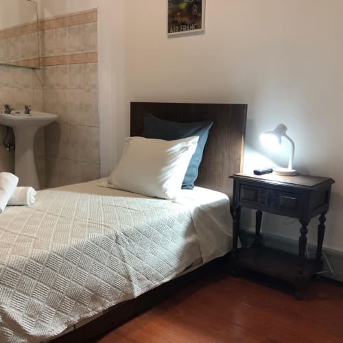 Quarto individual com cabeceira em madeira, roupa de cama branca e criado-mudo escuro na Pensão Infante Dom Henrique em Coimbra